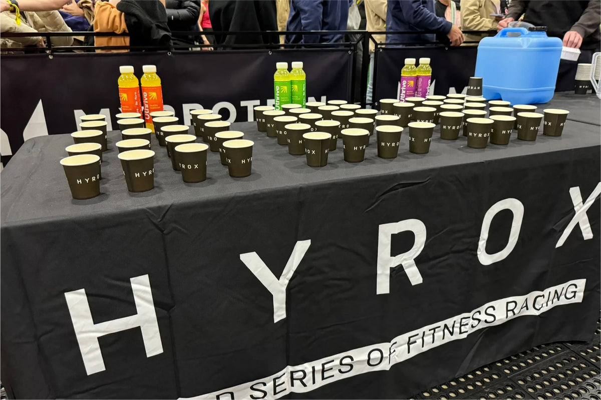 A sports hydration station featuring organized rows of drink cups and supplements at a HYROX fitness racing event.