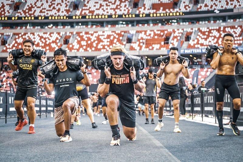 Athletes performing heavy sandbag lunges during a HYROX fitness racing event at the National Stadium in Singapore.