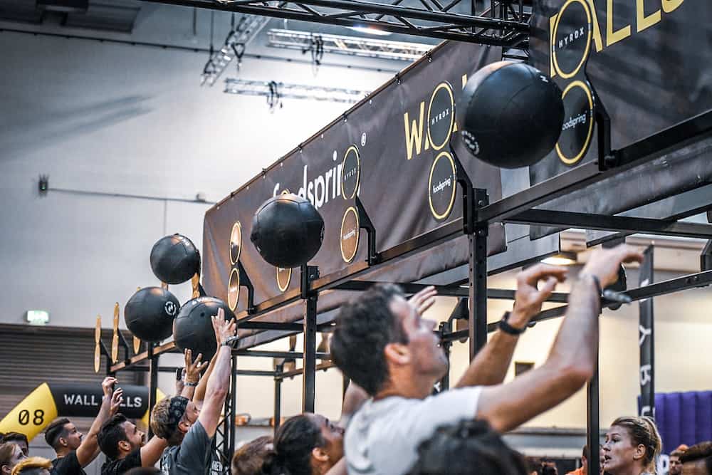 Athletes throwing heavy medicine balls at targets during a HYROX Wall Balls training session in Singapore.