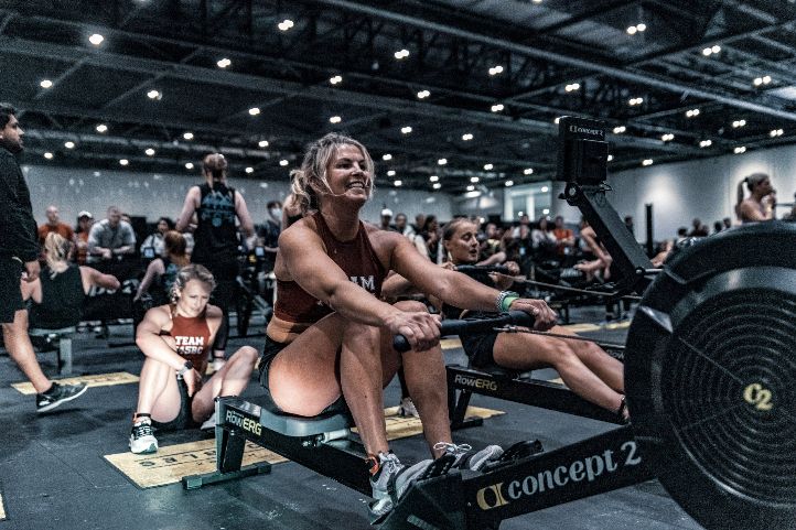 A smiling female competitor pulling the handle of a Concept2 rowing machine during a HYROX training event in Singapore.