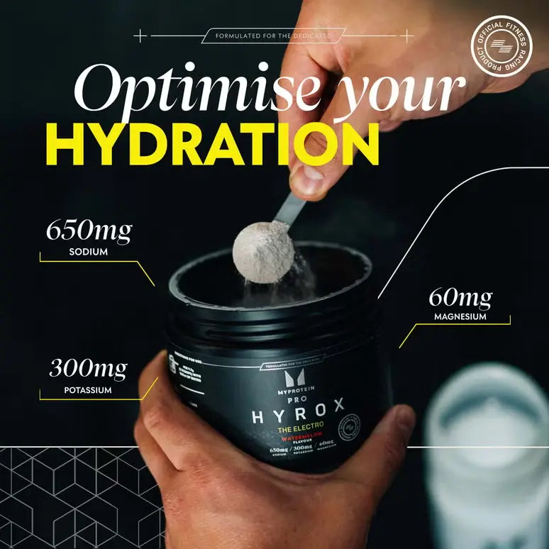 Scoop of Myprotein HYROX THE Electro powder above an open tub beside a water bottle
